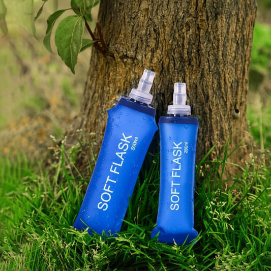 Two blue SOFT FLASKs on grass next to a tree